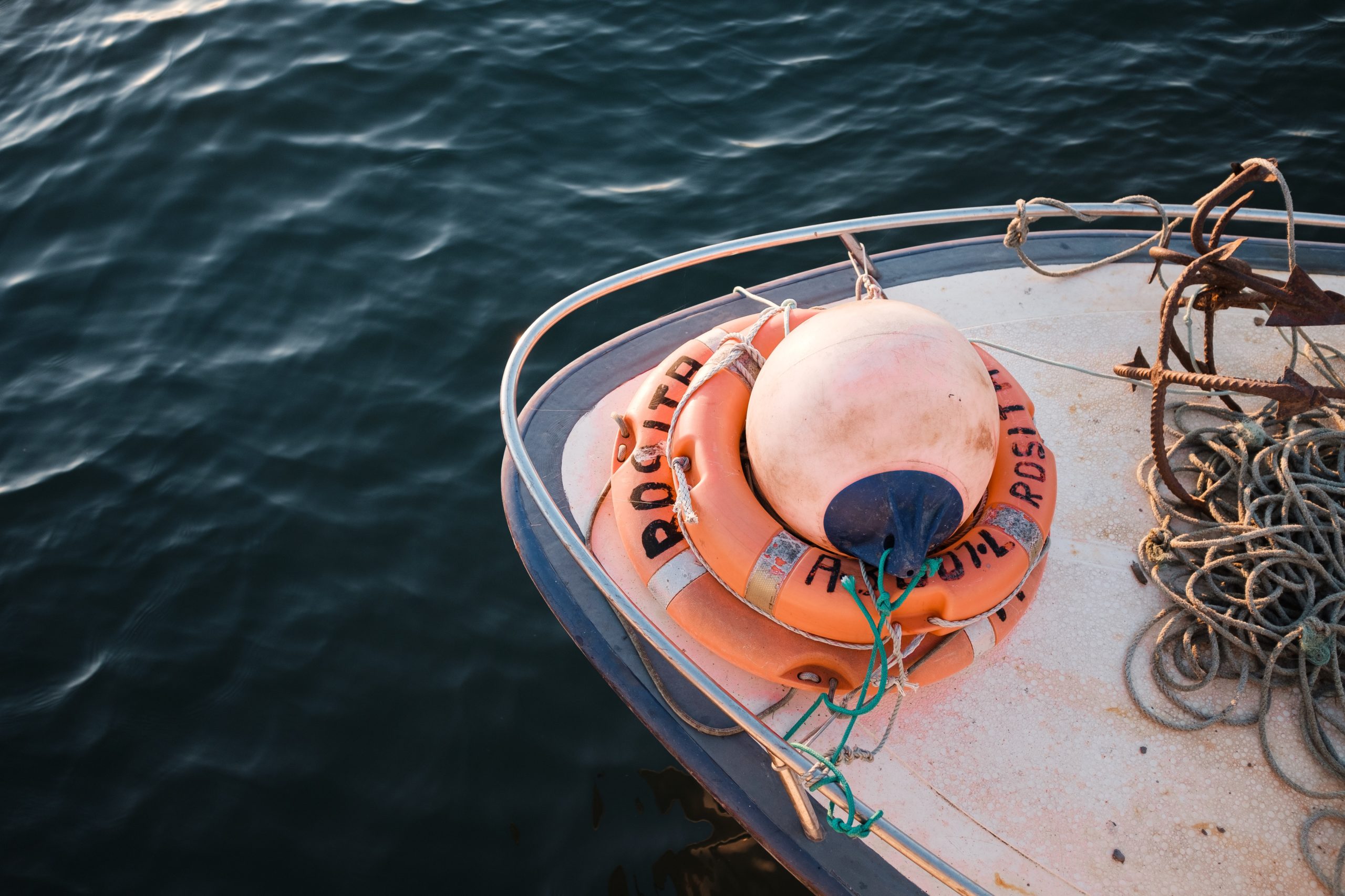 Boat deck with orange life ring and ropes on a calm water backdrop.