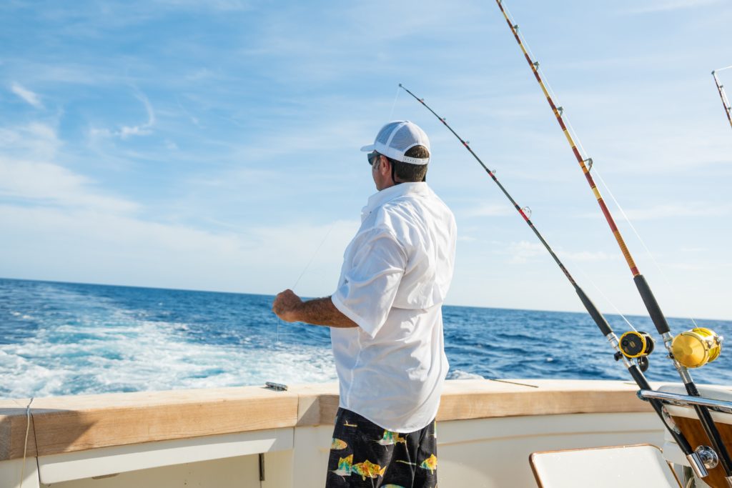 Man in white shirt and cap fishing on a boat at sea.