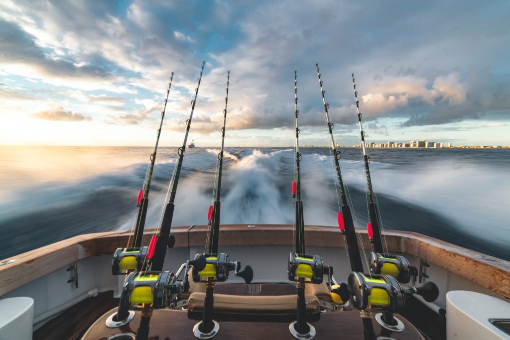 View from a boat with multiple fishing rods, speeding through water under a cloudy sky.
