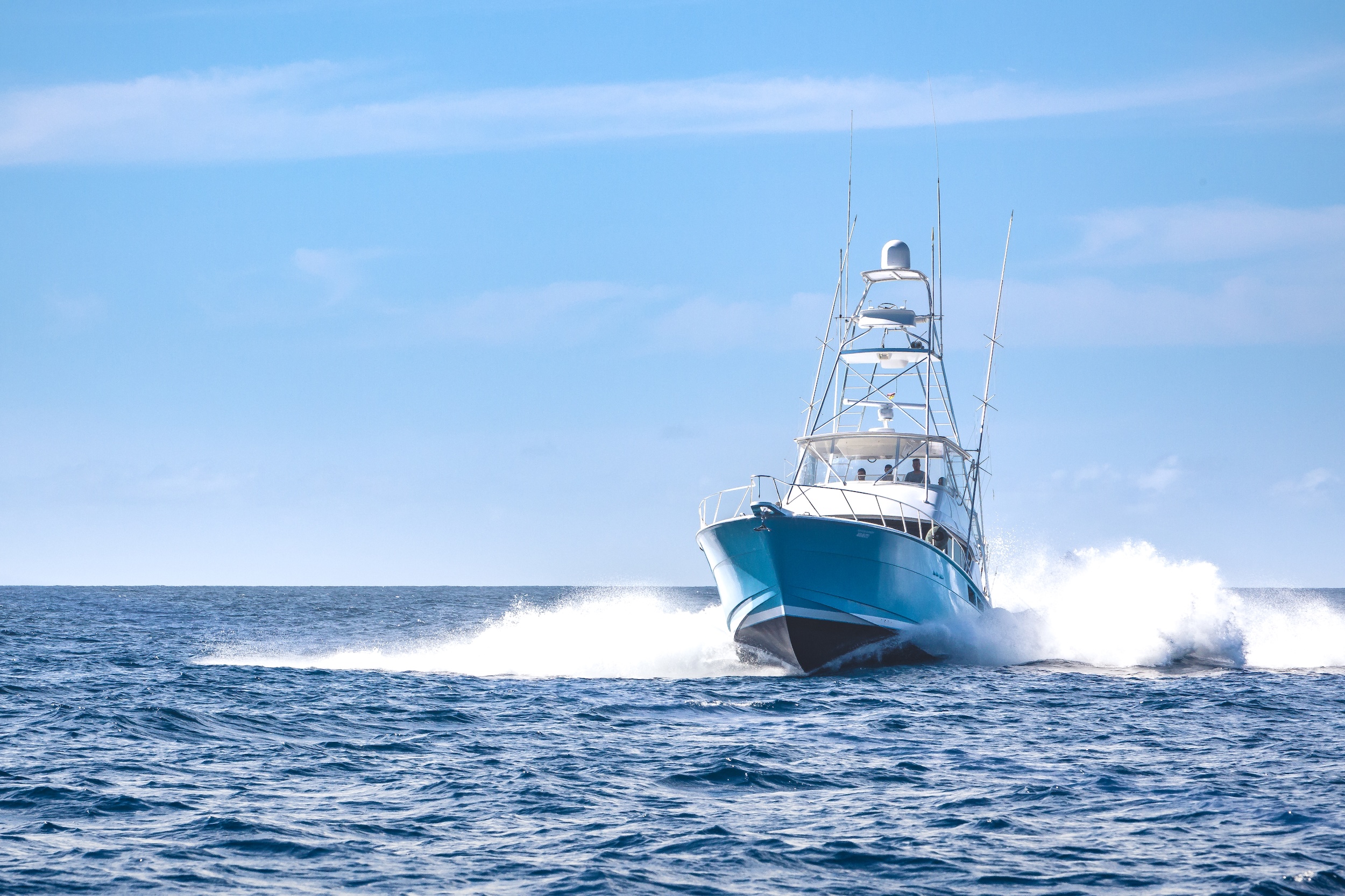 Boat speeding over open ocean, creating splashes under a clear blue sky.